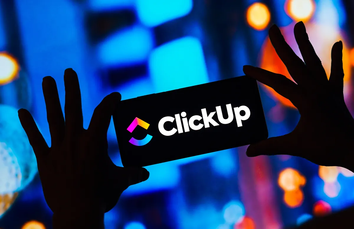 Símbolo e nome do ClickUp num painel de luz, com mãos em silhueta